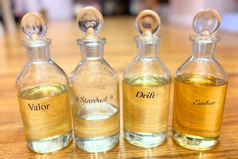 Four glass bottles with perfume oil labeled with the new fragrance names